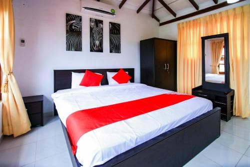 A cozy hotel room features a neatly made bed with red accents, framed zebra art on the walls, and warm yellow curtains, ideal for travelers seeking comfort and style in their accommodations.