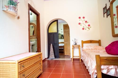A cozy bedroom with terracotta tiled floors, wooden furniture, and floral decorations exudes warmth and comfort, ideal for travelers seeking a charming and inviting accommodation.