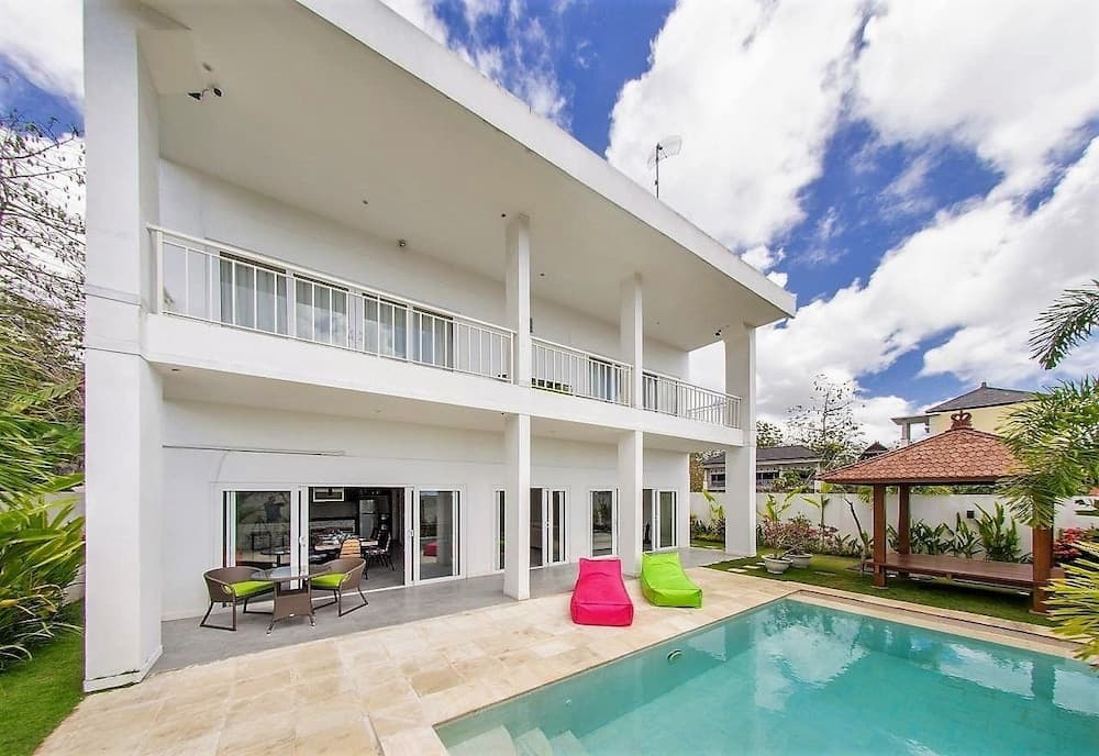 A serene tropical villa features a sparkling pool, colorful lounge chairs, and lush greenery under a bright blue sky, ideal for a luxurious vacation getaway.