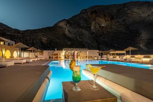 A serene evening at a luxurious poolside resort nestled against rugged cliffs, featuring inviting lounge chairs, colorful cocktails, and warm ambient lighting perfect for a romantic getaway.