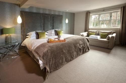 A cozy hotel suite features a plush bed with green accents, a comfortable seating area by the window, and soft lighting, ideal for travelers seeking relaxation and comfort.