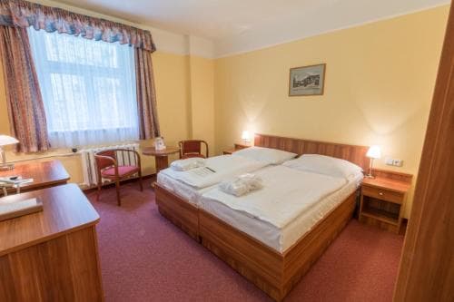 A cozy hotel room with warm yellow walls, a neatly made double bed, wooden furniture, and soft lighting creates an inviting atmosphere ideal for travelers seeking comfort and relaxation.