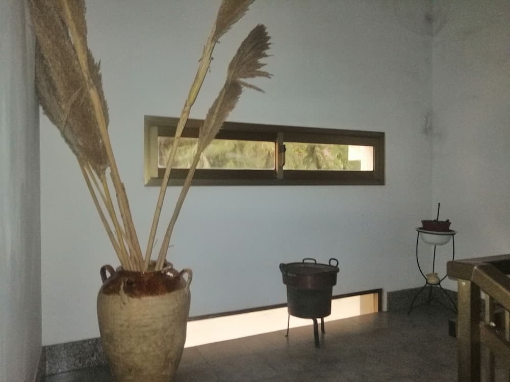 A serene indoor space features a rustic vase with dried reeds, a small window offering a glimpse of greenery, and minimalistic decor, ideal for travelers seeking a tranquil retreat.