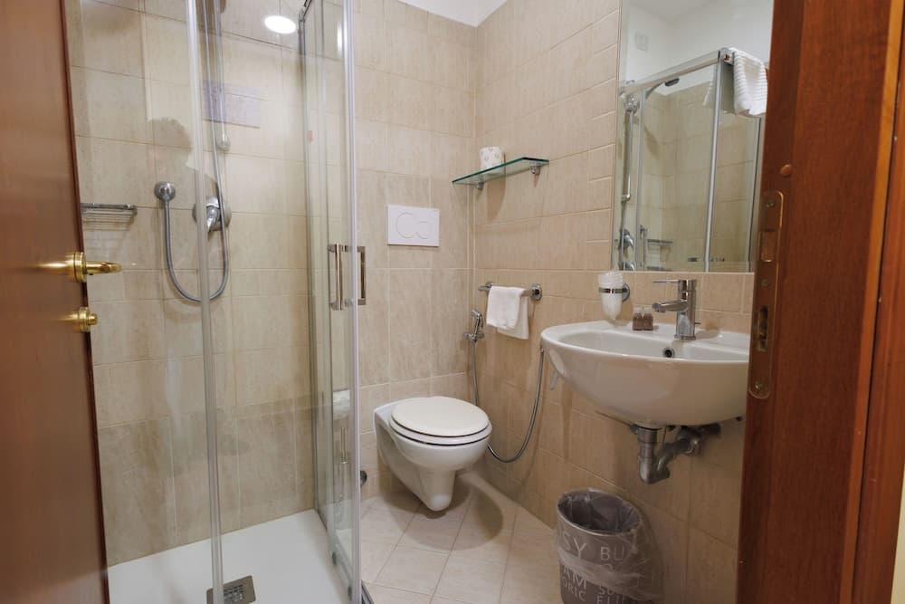 A cozy hotel bathroom features beige tiled walls, a glass-enclosed shower, a sleek sink, and a toilet, creating a clean and functional space ideal for travelers seeking comfort and convenience.