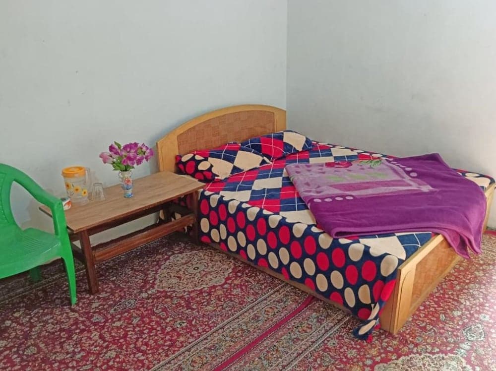 A cozy bedroom with a wooden bed adorned in colorful bedding, a vibrant rug, and a small table with flowers, ideal for travelers seeking a simple and welcoming accommodation.