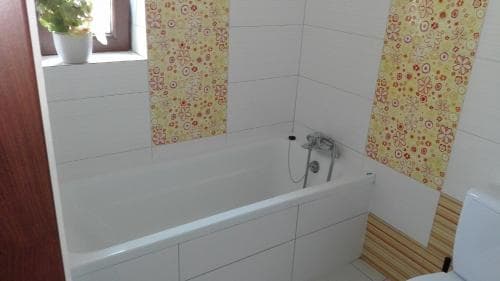 A cozy bathroom with white tiled walls, floral curtains, and a wooden floor exudes warmth and comfort, ideal for travelers seeking a relaxing retreat.