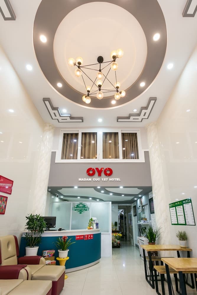 A modern hotel lobby features a stylish reception desk, cozy seating, and a chandelier under a circular ceiling design, creating an inviting atmosphere ideal for travelers seeking comfort and convenience.