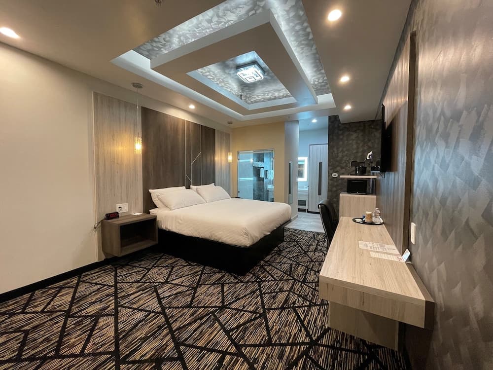 A modern hotel room features a cozy bed, sleek desk, geometric carpet, and stylish ceiling lights, ideal for travelers seeking comfort and contemporary design.