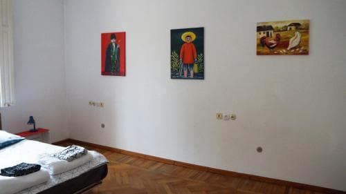 A cozy bedroom with artistic wall paintings creates a serene atmosphere, featuring a neatly made bed on wooden flooring, ideal for travelers seeking a culturally enriched stay.