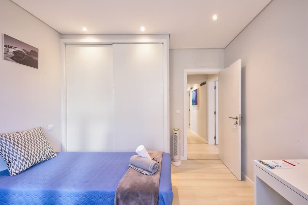 A cozy bedroom with a neatly made bed, modern sliding closet doors, and soft lighting creates a serene atmosphere ideal for travelers seeking a comfortable stay in a minimalist apartment.