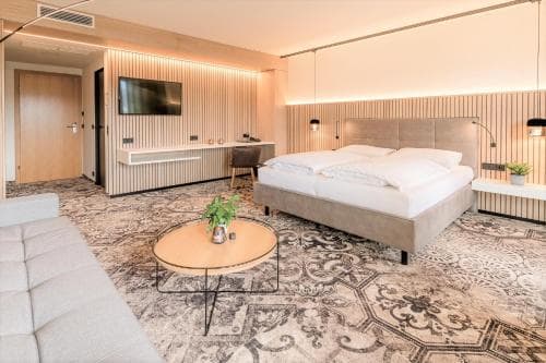 A modern hotel suite features a cozy bed, sleek furnishings, and ambient lighting, creating a serene atmosphere ideal for travelers seeking comfort and relaxation.