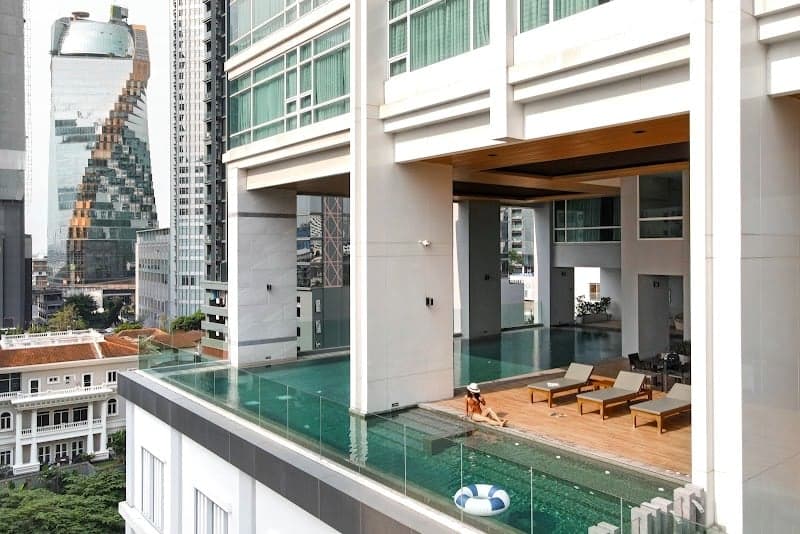 A serene rooftop pool at a modern hotel in Bangkok offers a tranquil escape with lounge chairs, a lifebuoy, and stunning views of the city's skyscrapers, perfect for travelers seeking relaxation amidst urban luxury.