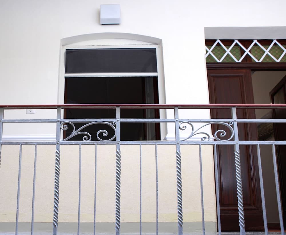 A serene balcony scene features ornate metal railings, a partially open window, and a decorative door, ideal for travelers seeking charming accommodation details.