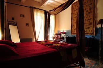 A cozy, warmly lit bedroom with rich red bedding, ornate curtains, and vintage decor creates an inviting atmosphere ideal for travelers seeking a charming and intimate accommodation experience.