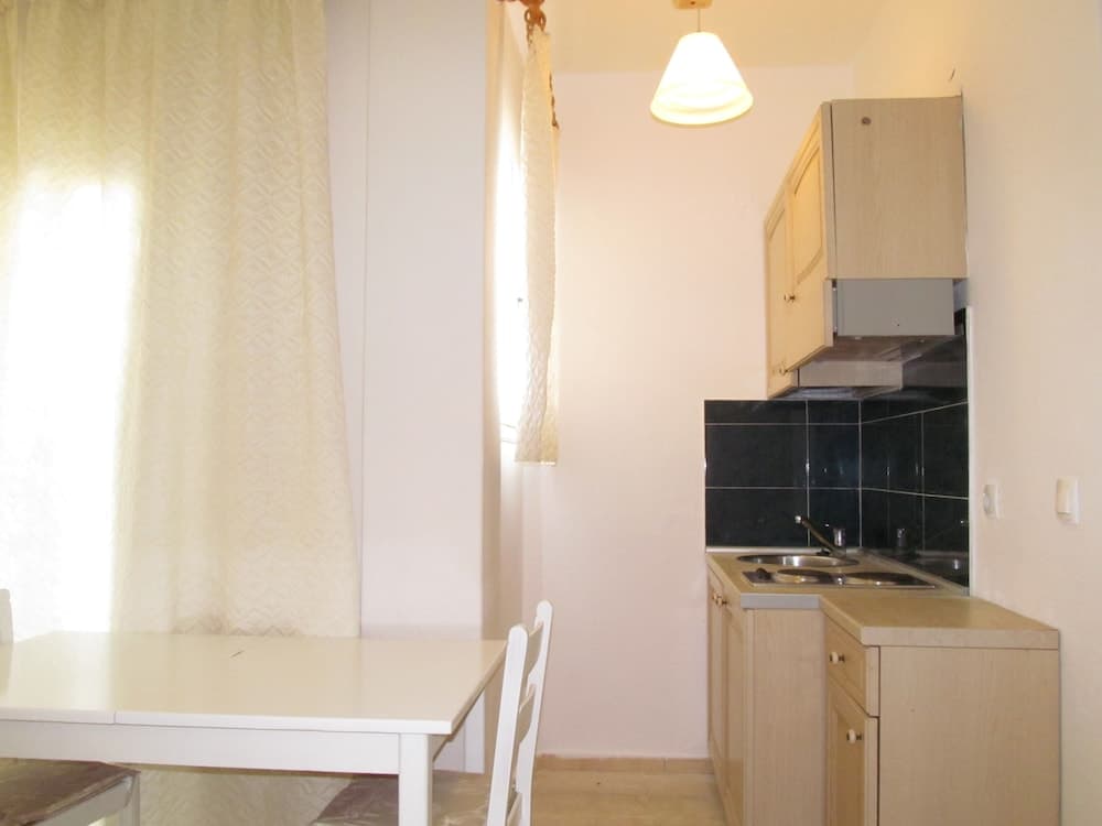 A cozy apartment kitchenette features light wooden cabinets, a black tiled backsplash, and a simple dining table by the window, ideal for travelers seeking a compact and functional living space.