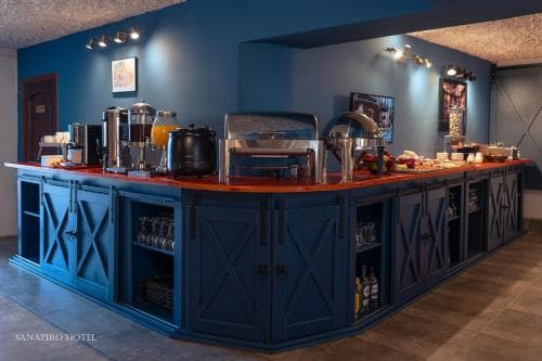 A cozy hotel buffet area features a stylish blue bar with red countertops, modern appliances, and warm lighting, creating an inviting atmosphere perfect for travelers seeking a comfortable dining experience.