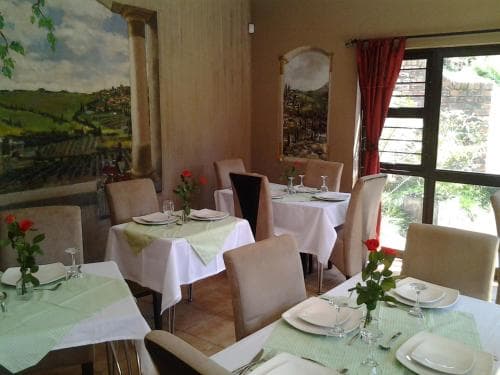 A cozy restaurant with rustic decor featuring landscape murals, set tables adorned with red roses, and large windows letting in natural light, ideal for travelers seeking a charming dining experience.