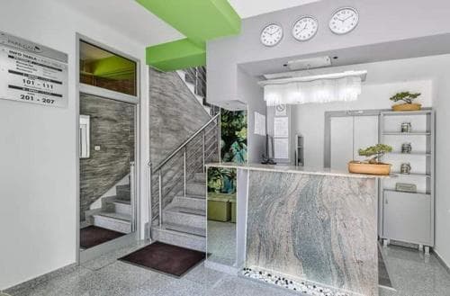 A modern hotel lobby features sleek marble accents, vibrant green ceiling panels, and a reception desk adorned with bonsai trees, creating an inviting atmosphere ideal for travelers seeking a stylish urban retreat.