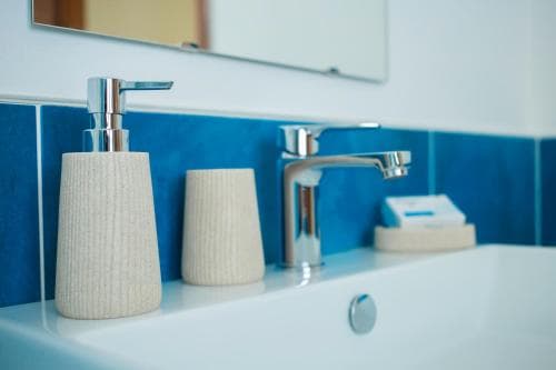 A serene hotel bathroom features a modern white sink with sleek chrome fixtures against a vibrant blue tiled backdrop, complemented by elegant beige accessories, ideal for travelers seeking comfort and style.