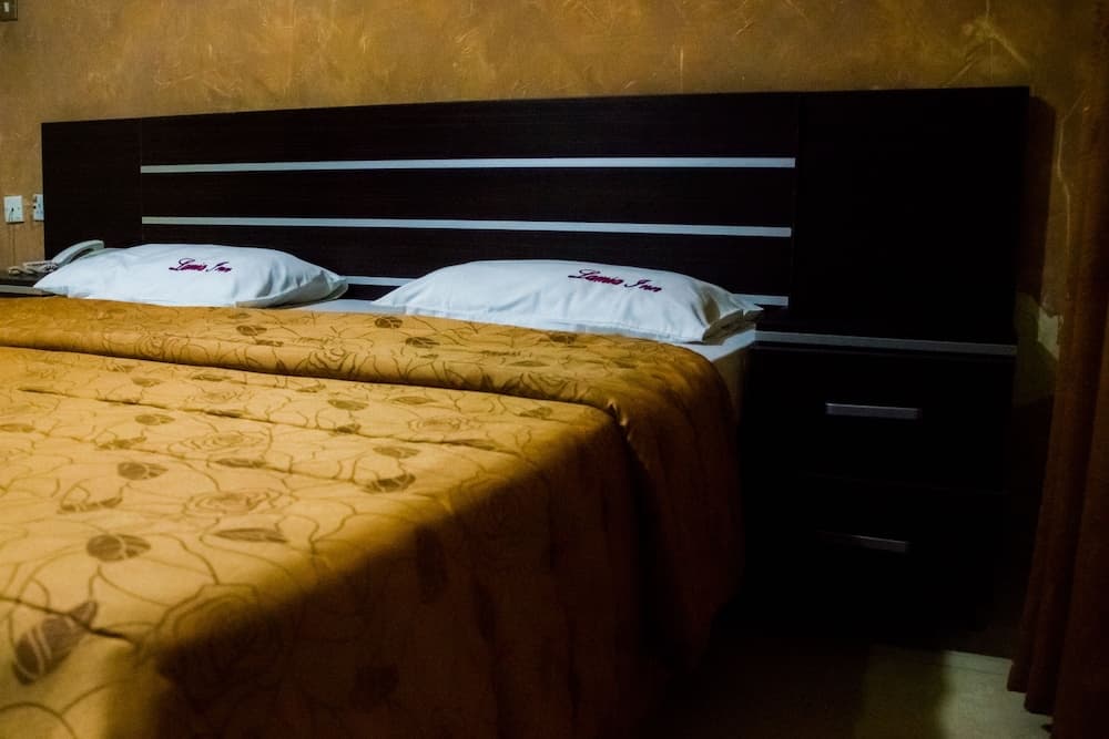 A cozy hotel room features two neatly made beds with patterned yellow bedding, white pillows embroidered with "Luna Inn," and a dark wooden headboard, ideal for travelers seeking comfort and simplicity.