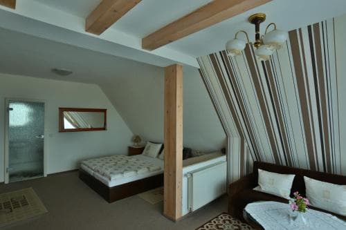 A cozy attic bedroom with wooden beams, striped curtains, and a comfortable bed offers a serene retreat for travelers seeking a charming and intimate accommodation experience.