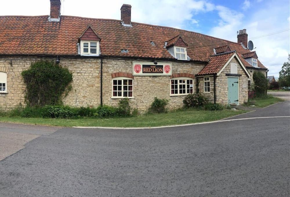 A charming stone pub with a red-tiled roof and "The Red Lion" sign offers a cozy rural retreat under a partly cloudy sky, ideal for travelers seeking a traditional English countryside experience.
