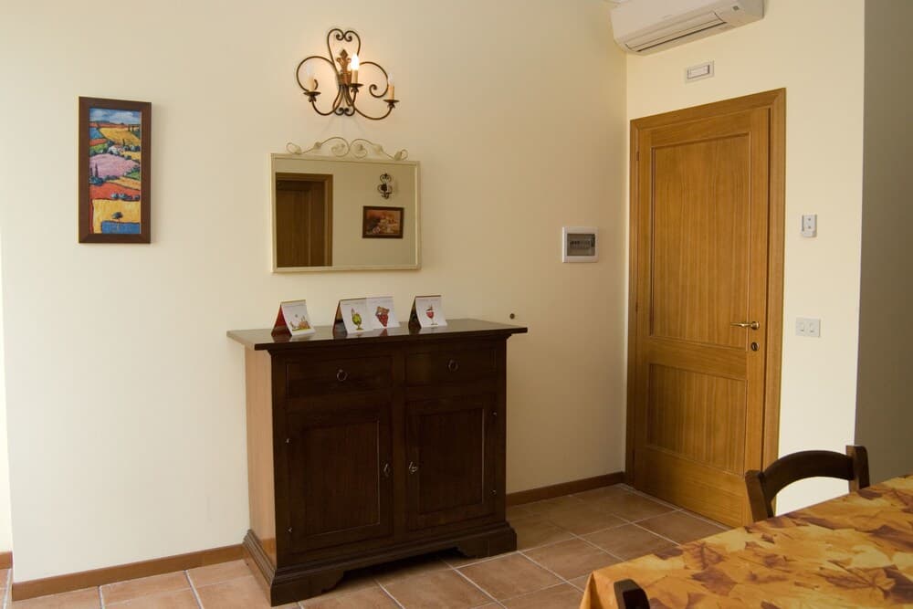 A cozy indoor dining area features a wooden sideboard adorned with cards, a mirror above it reflecting the warm ambiance, and a rustic tablecloth, ideal for travelers seeking a homely and inviting accommodation setting.