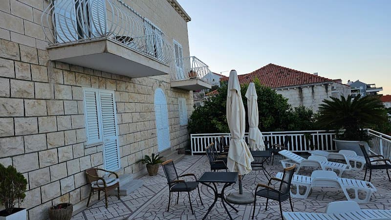 A serene outdoor terrace in Dubrovnik, Croatia, features cozy seating, closed umbrellas, and lush greenery against the backdrop of traditional stone buildings, ideal for travelers seeking relaxation and cultural immersion.