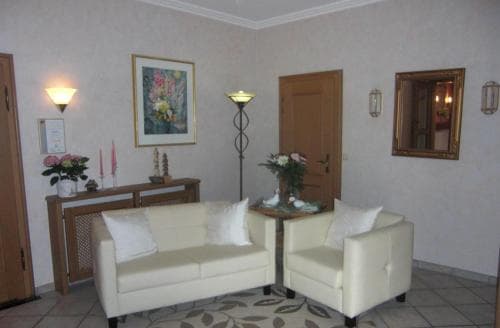 A cozy hotel lobby features cream-colored sofas, floral arrangements, and warm lighting, creating an inviting atmosphere ideal for travelers seeking relaxation.
