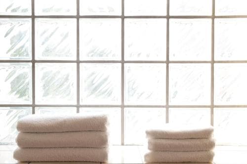 A serene spa setting features neatly stacked white towels against a backdrop of frosted glass windows, evoking a tranquil atmosphere ideal for relaxation and wellness retreats.