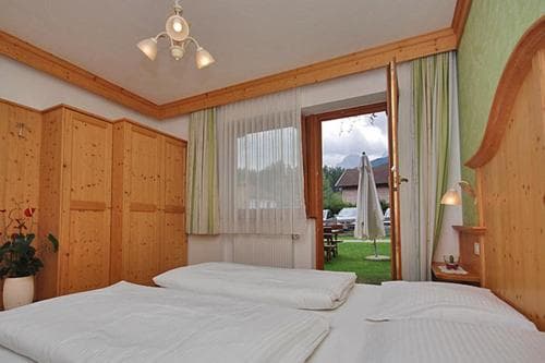 A cozy wooden bedroom with a view of lush greenery through an open door invites travelers seeking relaxation in a serene countryside retreat.