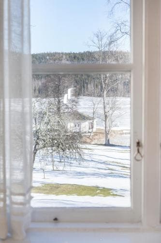 A serene winter landscape viewed through a cozy window, featuring snow-covered fields, bare trees, and distant hills, evokes a peaceful retreat ideal for travelers seeking tranquility in nature.