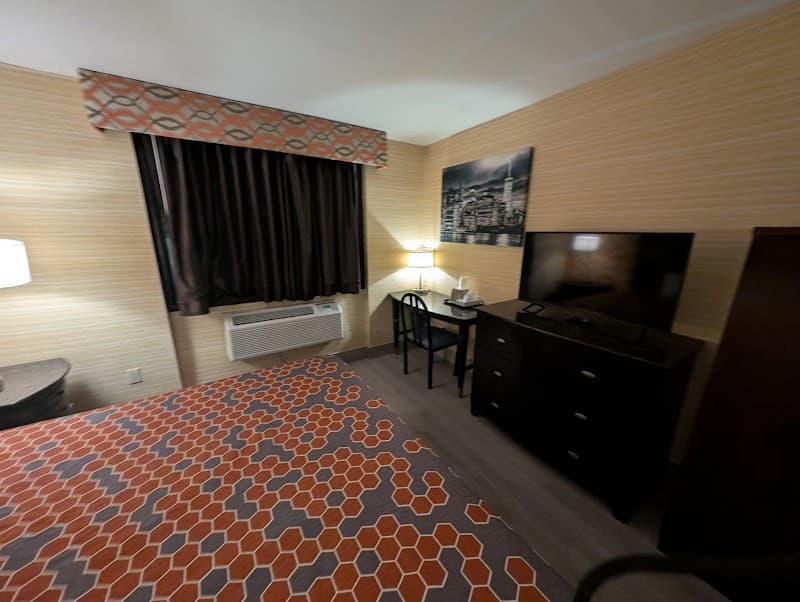 A cozy hotel room in Corona, NY features a patterned bedspread, striped walls, and a desk setup, ideal for travelers seeking comfort and functionality during their stay.