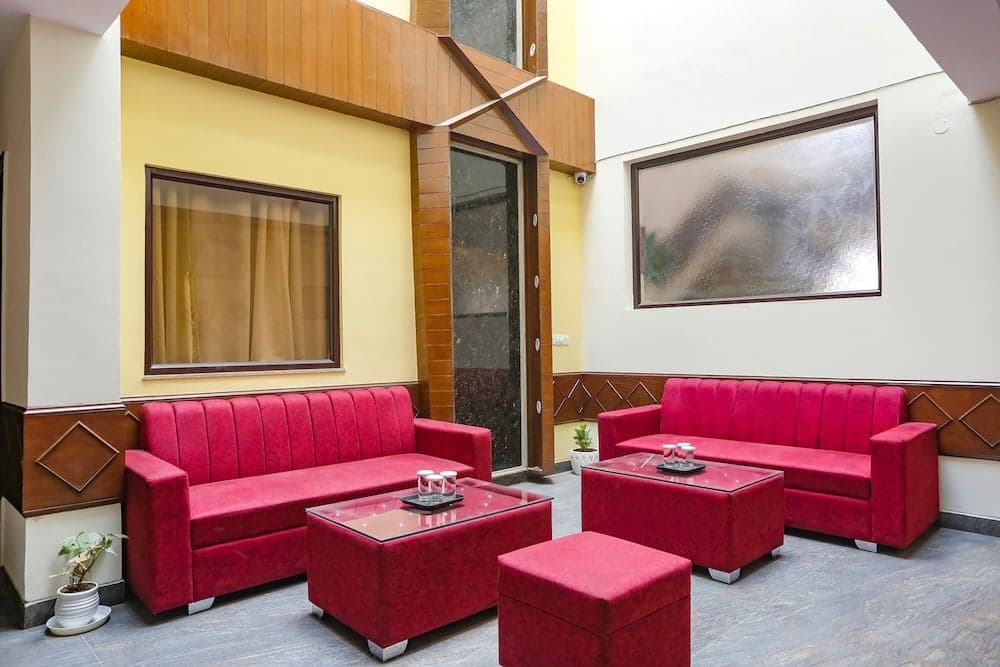 A cozy hotel lobby features vibrant red sofas arranged around glass-top tables, set against warm yellow walls adorned with wooden accents and framed artwork, ideal for travelers seeking a comfortable and inviting atmosphere.