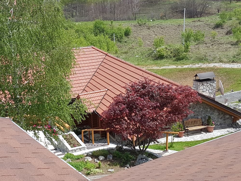 A serene countryside retreat features a charming stone cottage with a red-tiled roof, surrounded by lush greenery, vibrant red foliage, and a cozy wooden bench, ideal for travelers seeking a peaceful rural getaway.