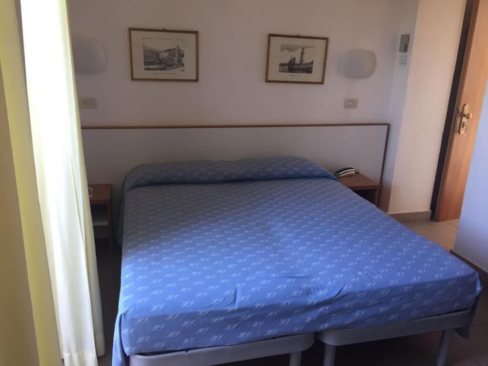 A cozy hotel room features a neatly made bed with blue bedding, framed artwork on the wall, and wooden bedside tables, ideal for travelers seeking a simple and comfortable stay.