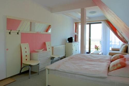 A cozy attic bedroom with soft pink accents, white furniture, and a balcony view offers a serene retreat for travelers seeking a charming and intimate accommodation experience.