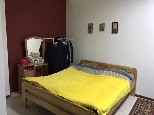 A cozy bedroom with a wooden bed draped in a bright yellow blanket, a vanity mirror on a small dresser, and framed pictures on the wall, ideal for travelers seeking a simple and comfortable accommodation.