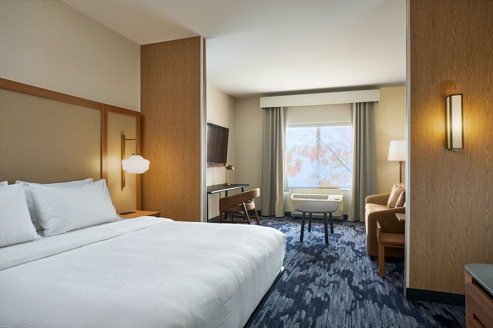A cozy hotel room features a neatly made bed, modern furnishings, and a window view of autumn leaves, ideal for travelers seeking comfort and relaxation.