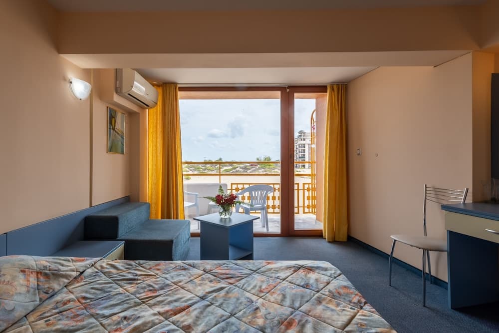A cozy hotel room with a vibrant balcony view of the sea, featuring yellow curtains, modern furnishings, and a serene atmosphere ideal for travelers seeking relaxation by the coast.