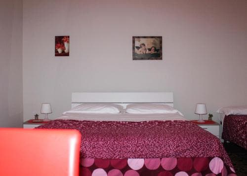 A cozy hotel room features a neatly made bed adorned with vibrant pink bedding and heart-patterned decor, framed by soft lighting from bedside lamps, ideal for travelers seeking a romantic getaway.