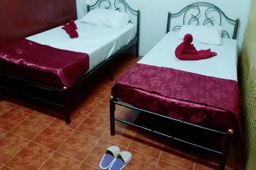 A cozy budget-friendly hotel room features two neatly made single beds with red accents and decorative towels, set on tiled flooring, ideal for travelers seeking simple accommodations.