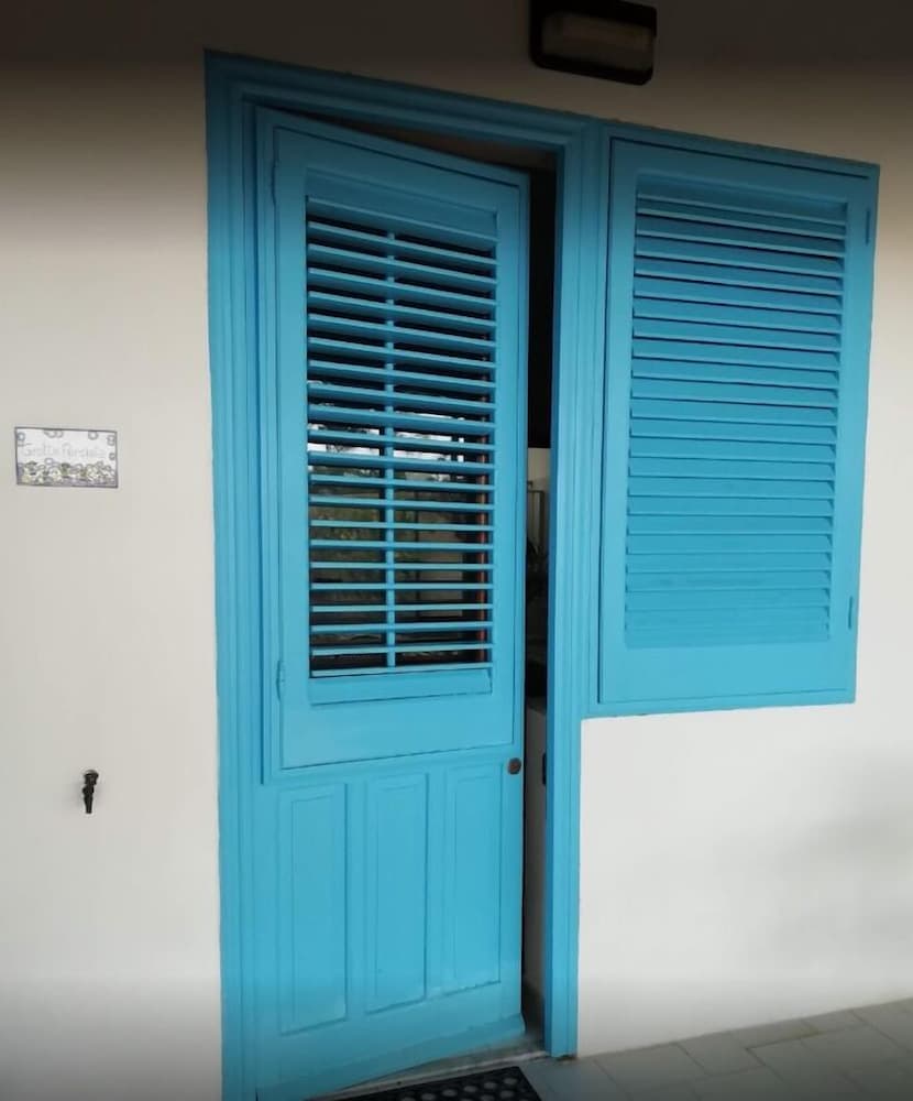 A serene coastal villa entrance features a charming turquoise shuttered door against a white wall, ideal for travelers seeking a peaceful retreat.