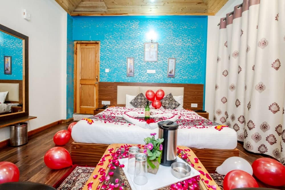 A cozy hotel room with vibrant blue walls, wooden accents, and romantic decorations including red balloons and rose petals, ideal for a honeymoon or special occasion getaway.