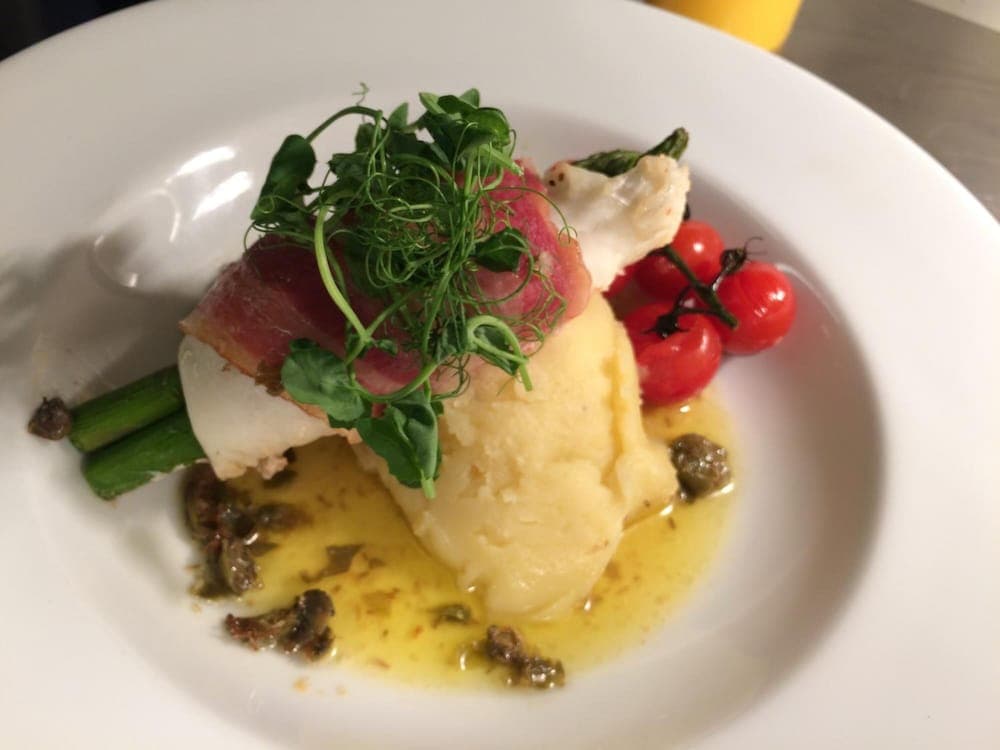 A beautifully plated gourmet dish featuring mashed potatoes, seared tuna, cherry tomatoes, and microgreens on a white plate, perfect for a fine dining experience or culinary travel enthusiasts.