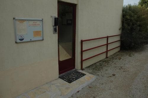 A serene entrance to a guesthouse features a welcoming door, informational board, and red railing, ideal for travelers seeking a cozy rural retreat.