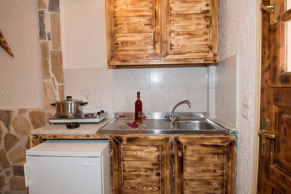 A cozy rustic kitchen with wooden cabinets, tiled backsplash, and a small sink setup featuring a bottle of wine and glasses, ideal for travelers seeking a charming self-catering retreat.