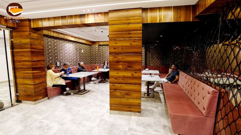 A cozy indoor café with wooden paneling, plush pink sofas, and patrons enjoying conversations creates an inviting atmosphere ideal for travelers seeking a relaxing spot to unwind and socialize.