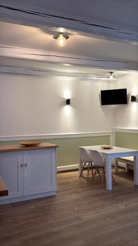 A cozy, modern dining area with wooden floors, white cabinetry, and a mounted TV creates an inviting atmosphere ideal for travelers seeking a comfortable space for meals or gatherings.
