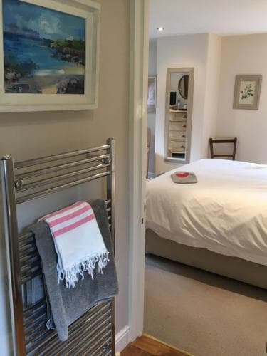 A cozy bedroom with a neatly made bed, framed artwork, and a towel-warmed radiator creates a serene retreat, ideal for travelers seeking comfort and relaxation.